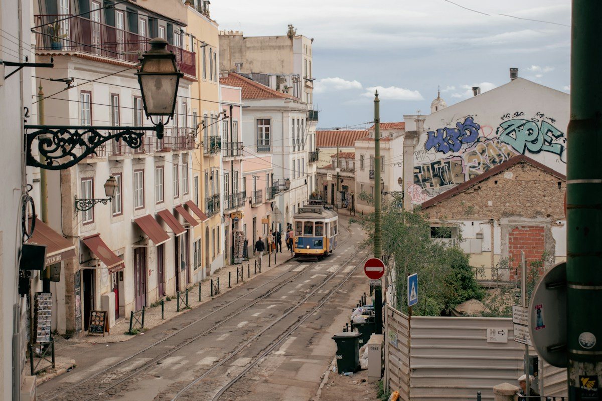A yellow Lisbon tram passing through a narrow street.