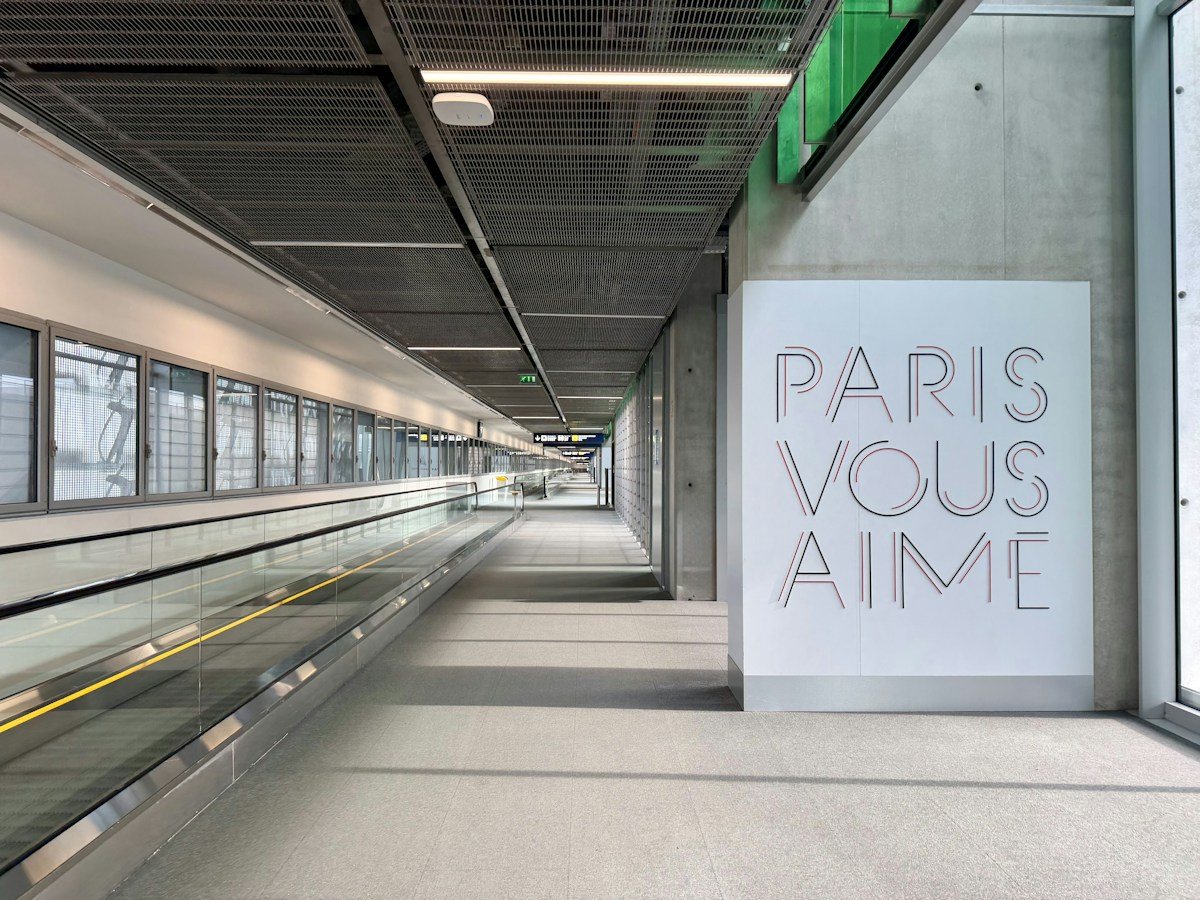 A terminal walkway at Paris Charles de Gaulle Airport with a Paris vous aime sign.