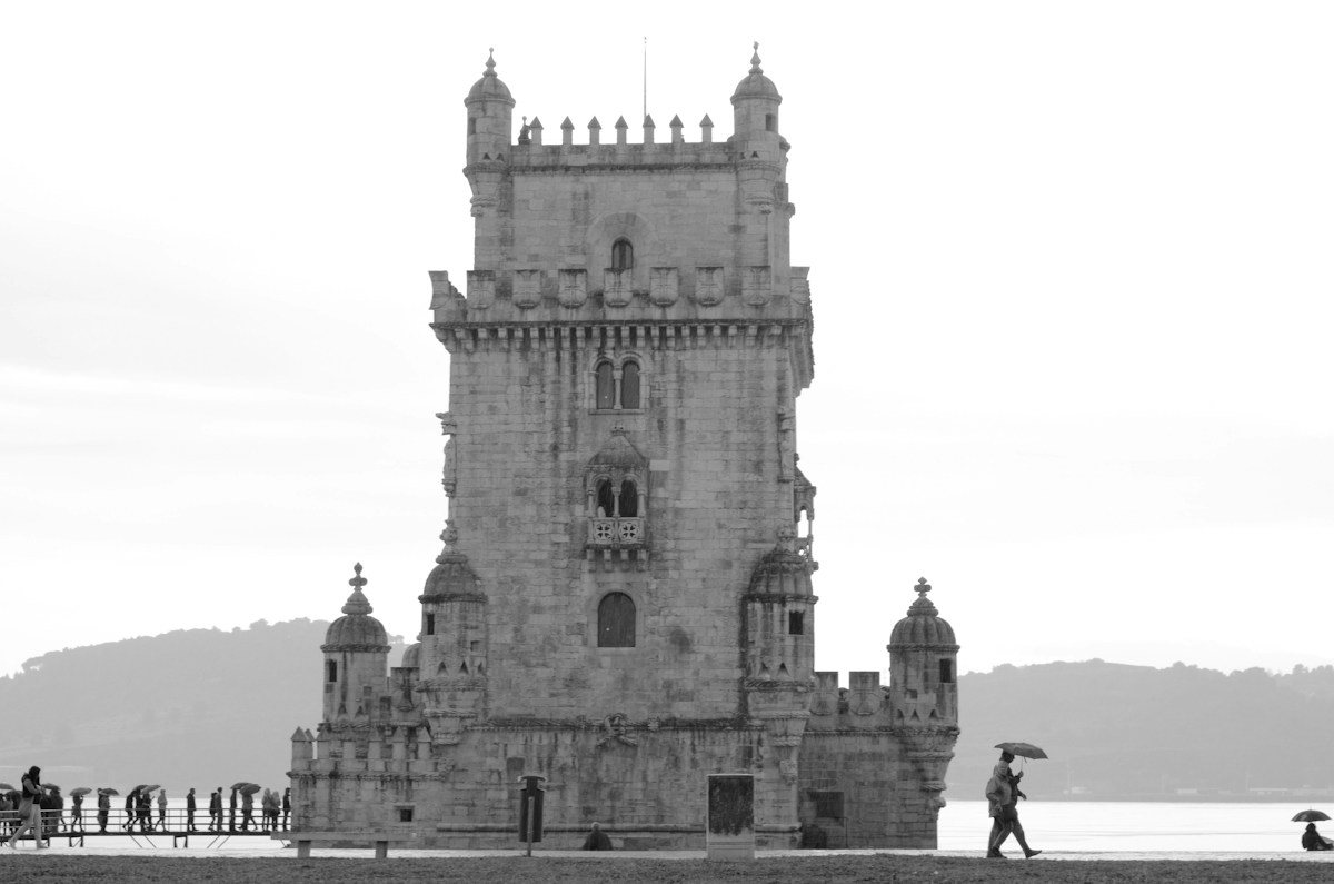 Black and white view of Belem Tower with umbrellas on a rainy day.